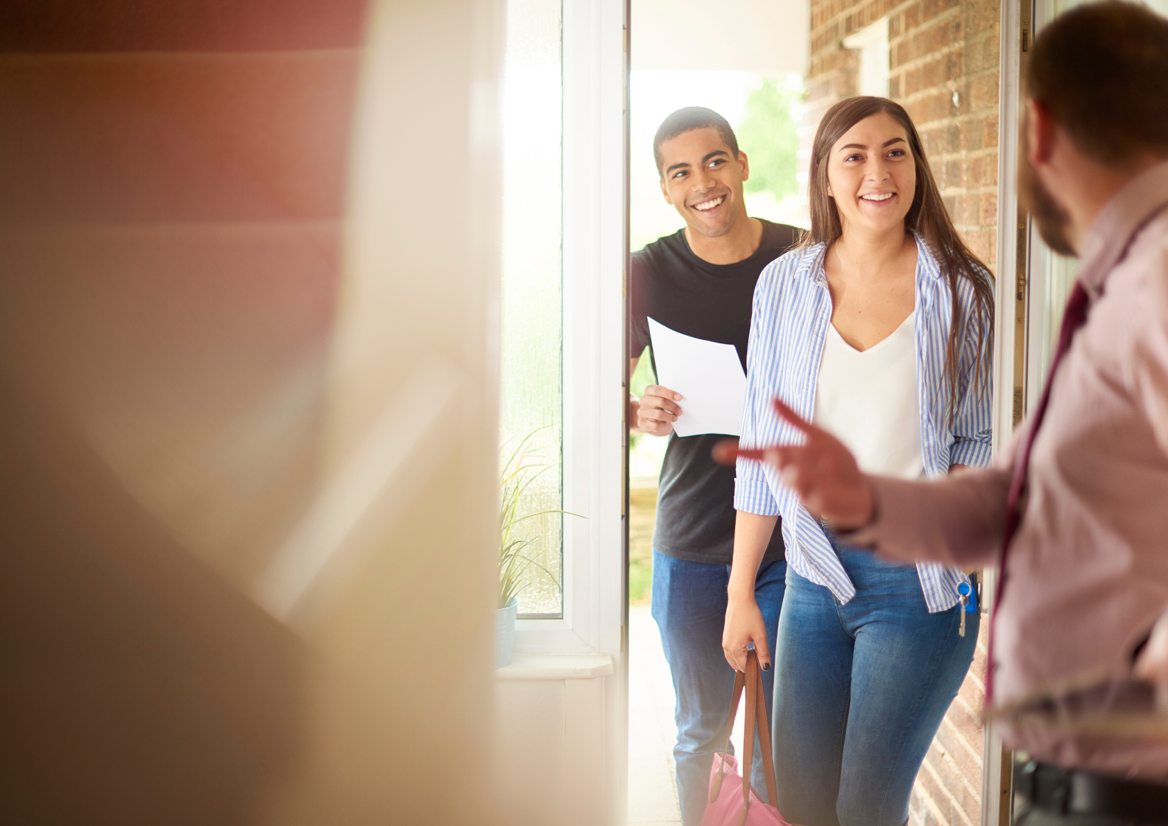 young couple walking into an open house welcomed by a realtor. 