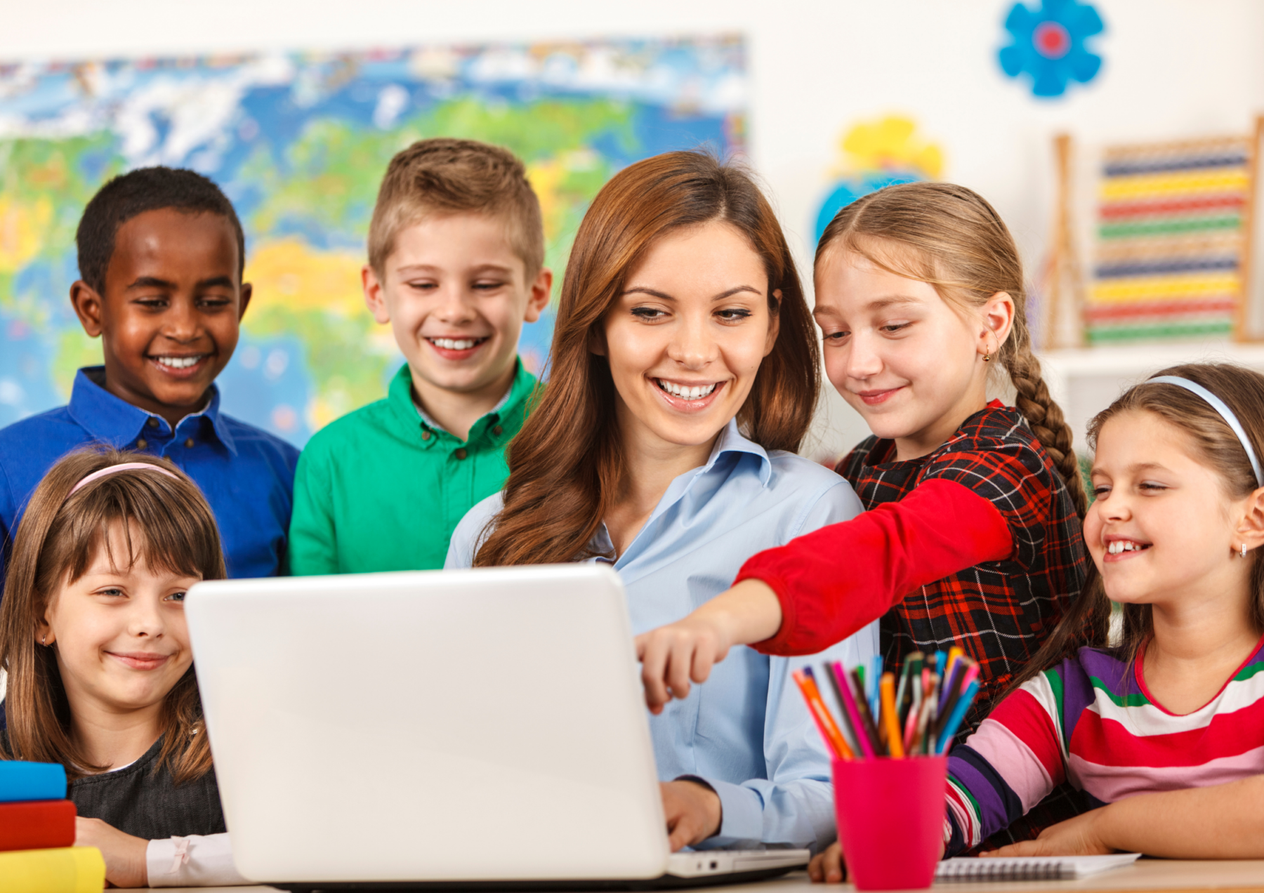 teacher on a lap top surrounded by students in a classroom.