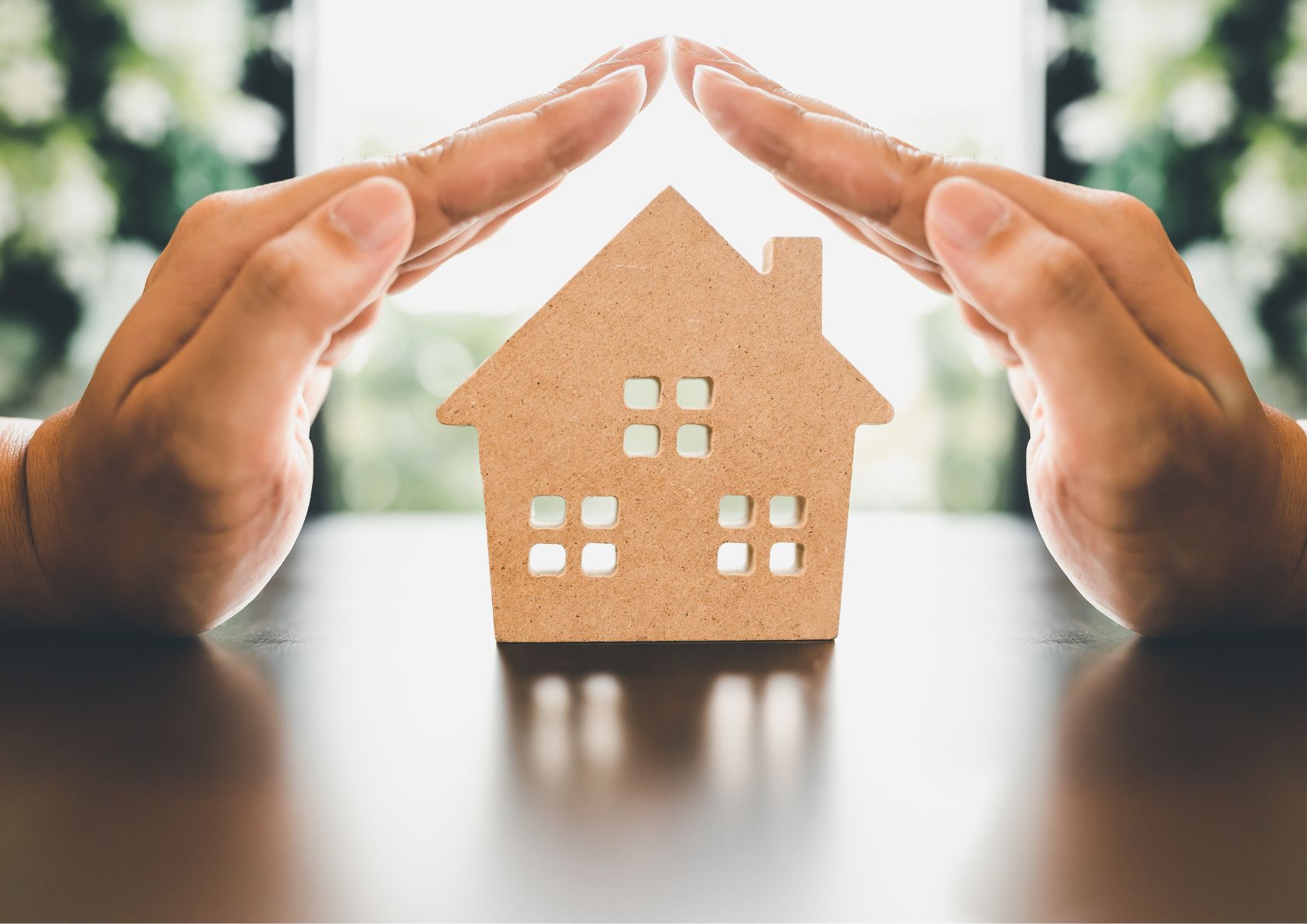 a cutout of a home with hands protecting it. First time homebuyers or foreclosure home buying. 