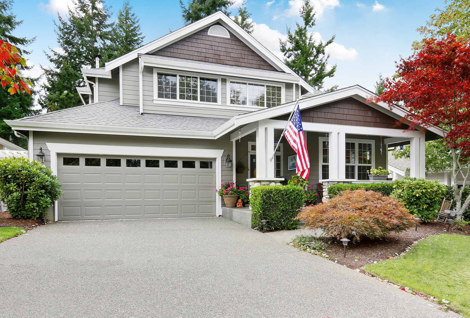 Nice curb appeal of grey house with garage and driveway. Column porch with American flag. Northwest USA