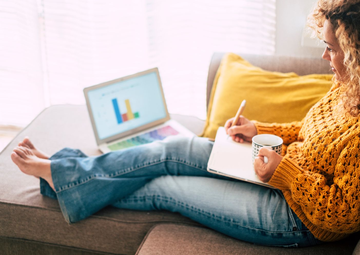 A woman staying on top of current real estate trends while drinking coffee on her couch.