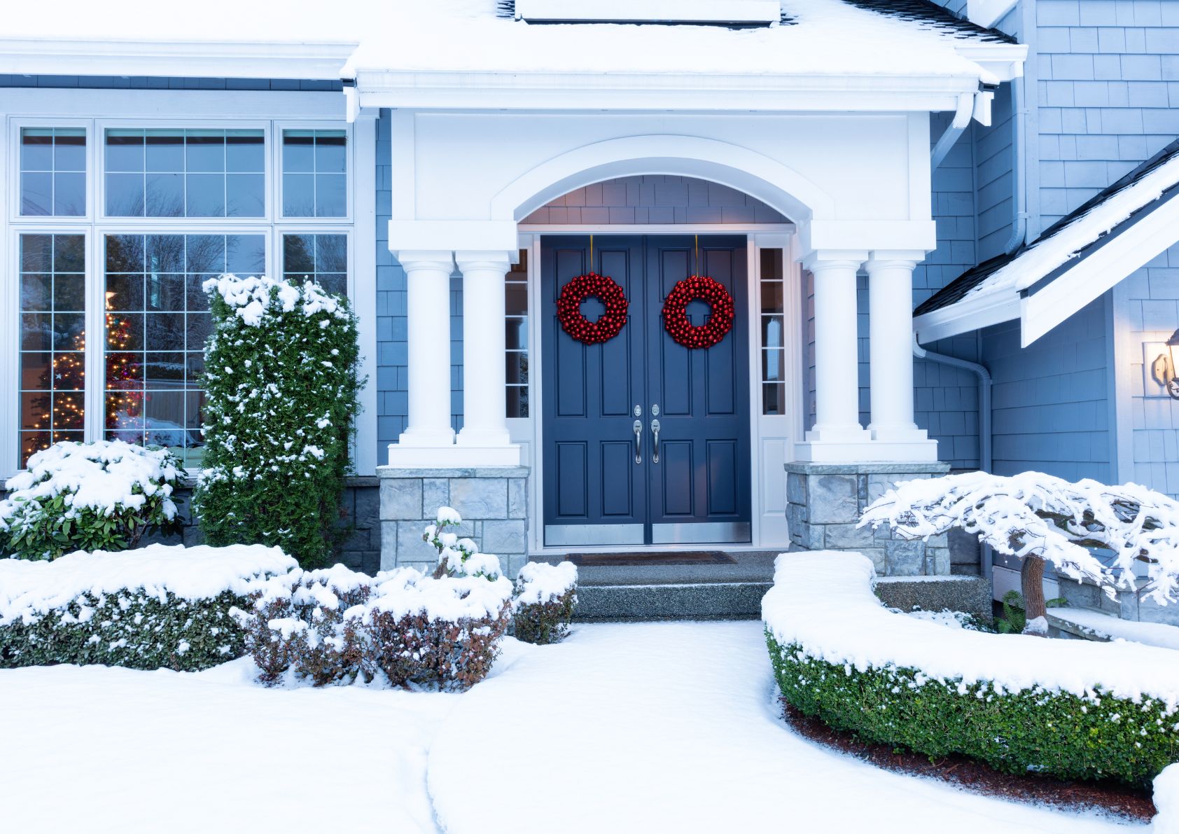 Home exterior with a close up on the doorway decorated for the holidays and covered in snow. 